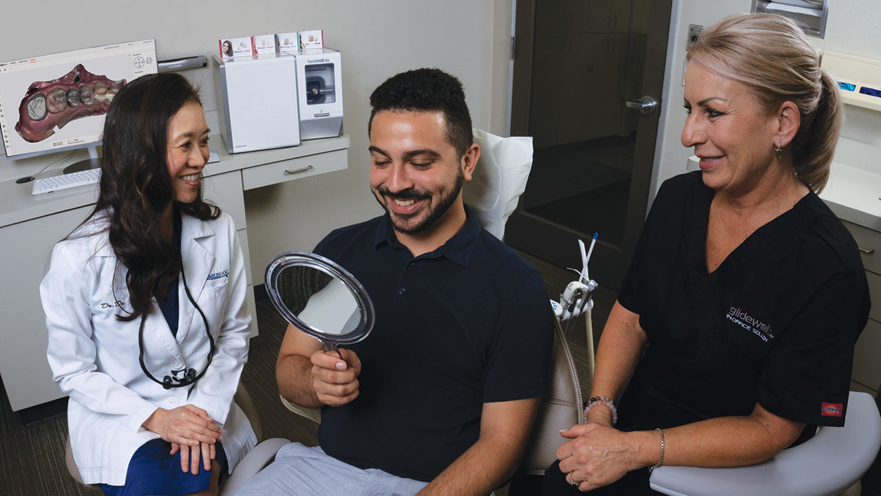 A patient checking his teeth on a mirror with dental staff