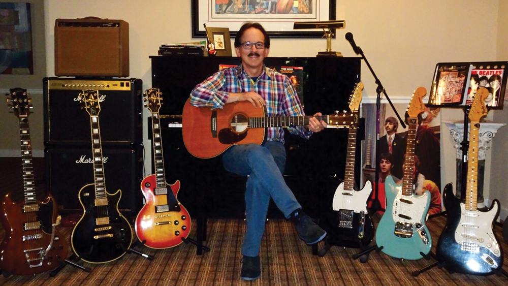 Dr. David Hochberg sitting with his collection of guitars