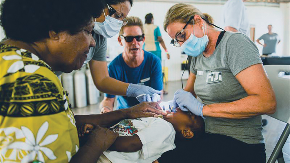 A young boy comforted by a family member receives dental treatment from a volunteer pediatric dentist