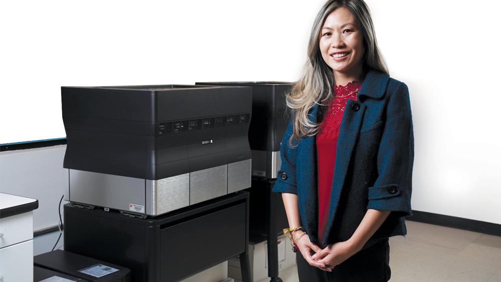 Mui is standing in front of the 3D printers used to fabricate surgical guides based on digital treatment plans she develops in collaboration with dentists