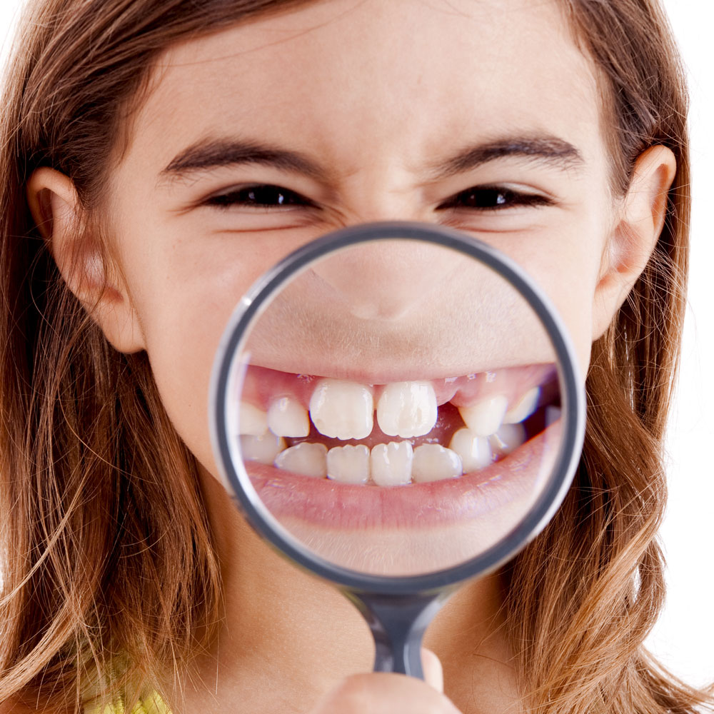 Girl holding magnifying glass on her teeth